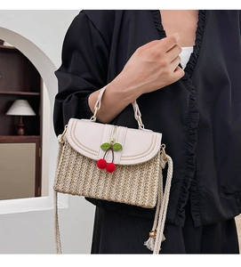 Detail of handwoven straw bucket bag with white leather flap and 3D cherry ornament