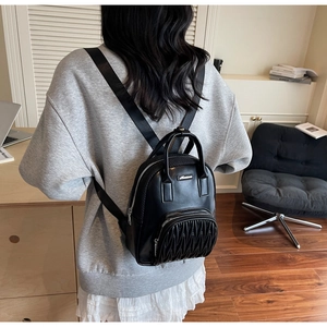 Detail of black mini backpack featuring pleated texture front pocket and metal logo plaque