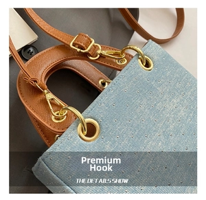 Detail of light blue denim textured bag featuring brown leather handles and gold metal rings