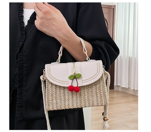 Detail of hand-woven straw bag with white leather flap and red cherry pendant charm