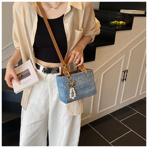 Blue denim crossbody bag with brown leather handles and a decorative pearl charm