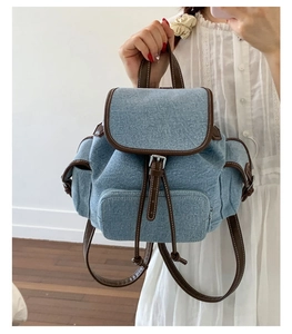 Detail of light blue denim backpack with brown leather trim and magnetic buckle straps