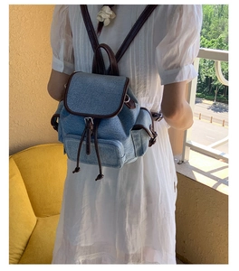 Rear view of a light blue denim backpack with brown leather trim worn by a model