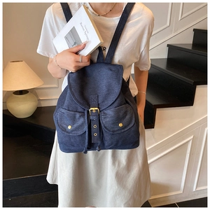 Detail of dark blue denim backpack featuring metal buckles and symmetric front pockets