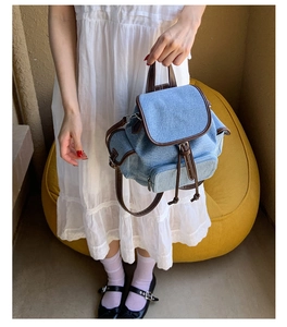 Detail of vintage light blue denim backpack with brown leather trim and drawstring closure