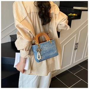 Detail view of denim handbag featuring premium brown leather handles and pearl bow charm