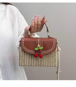 Detail of straw woven box bag with brown leather trim, tassels, and cherry pendant