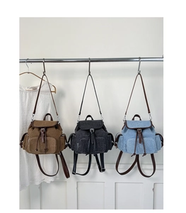 Three canvas backpacks in brown, black, and denim blue hanging on a metal rack