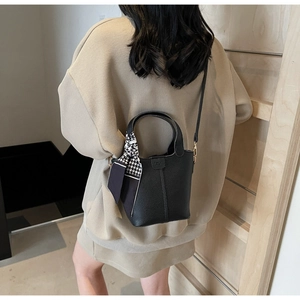 Detail of black pebbled leather bucket bag featuring a houndstooth silk scarf on the handle