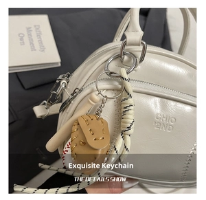 Detail of baseball charm with leather glove and wooden bat on a white handbag
