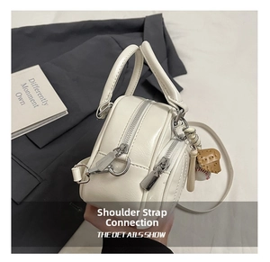 Close-up of a white mini pillow bag featuring dual zippers and a baseball bat charm