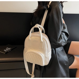 Side view of a beige quilted mini backpack worn by a model in a black leather jacket