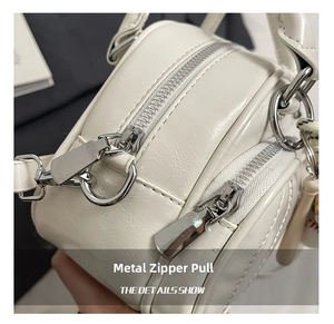 Detailed view of silver metal zipper pulls and white textured leather on a pillow bag