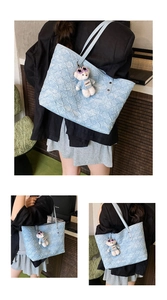 Detail of light blue textured tote bag with a white plush bear charm and long leather straps