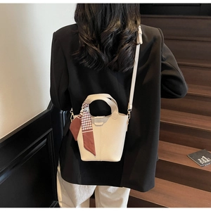 Detail of off-white bucket bag with houndstooth scarf handle on a wooden staircase