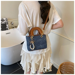 Detail of blue denim crossbody bag featuring pearl charm and brown leather handles