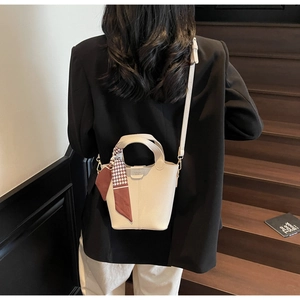 Chic off-white bucket bag with silk scarf accessory worn by model on a wooden staircase