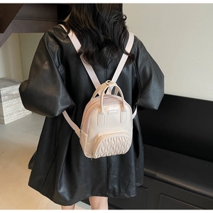 Detail of ruffled beige mini backpack featuring mesh texture and metal brand plaque