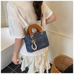Detail of blue denim polka dot handbag with leather handles and pearl bow charm