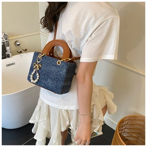 Close-up of blue denim polka dot tote bag with brown leather handles and pearl bow charm