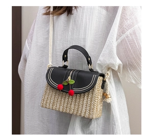 Detail of straw woven bag with leather lid, cherry charms and cotton rope shoulder strap