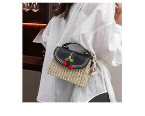 Detail of woven straw box bag with black flap and cherry pompom charms for summer