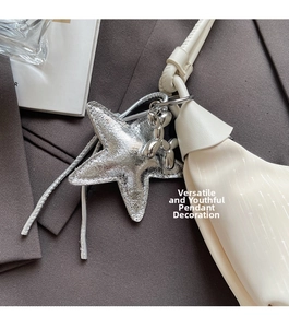 Detail of silver star and balloon dog charms on a beige crescent-shaped shoulder bag
