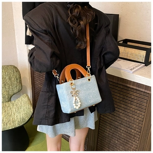 Detail of light blue denim handbag with brown leather ring handles and pearl bow charm