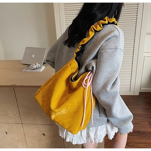 Detail of yellow tote bag featuring ruffled strap and pink drawstring side accents