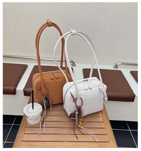 Detail view of brown and white crossbody bags with knotted charms on a wooden bench