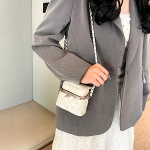 Detail of white quilted crossbody bag with sparkling rhinestones and metal clasp closure