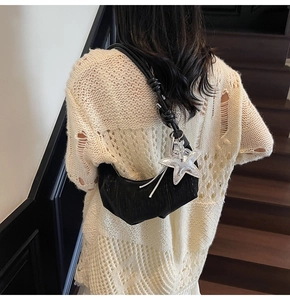 Detail of black crescent shoulder bag with a large silver star pendant on wooden stairs