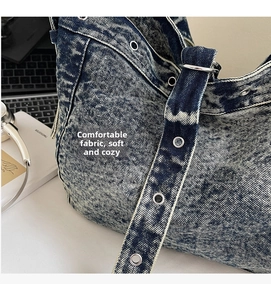 Detail view of blue acid wash denim tote bag showing metal eyelets and wide buckled strap