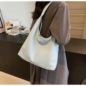 Pale blue pebbled leather tote bag worn by a model in a modern urban office setting