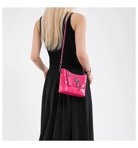 Detalle de bolso rosa con textura de cocodrilo, cruz de plata y cadena decorativa