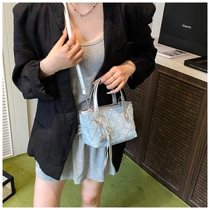 Close-up of light blue quilted mini bucket bag with silver metal handle and fringe detail