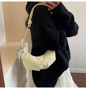 Detail of light yellow crescent bag with knotted shoulder strap and silver butterfly charm