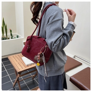 Detail of burgundy suede tote bag featuring white contrast stitching and bow ornament