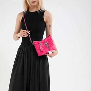 Hot pink croc-effect crossbody bag with silver cross detail and chain strap on a model