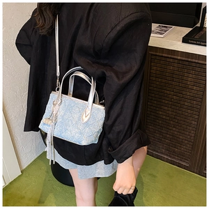 Detail of light blue wrinkled crossbody bag with silver handle and tassel on black suit