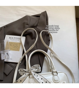 Borsa in pelle lucida bianca con foulard a pois su letto con blazer marrone