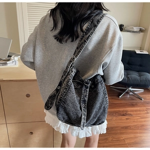 Rear view of a large black acid wash denim tote bag worn by a model in a bright room