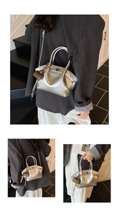 Close-up of a silver metallic trapezoid tote bag with brown leather charm on a stair