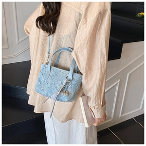 Detail of light blue pleated handbag with lace ribbon and metallic chain pendant charm