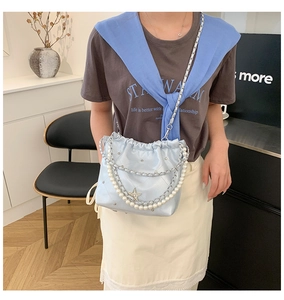 Détail du charm étoile et de la chaîne en perles sur le sac seau matelassé bleu clair