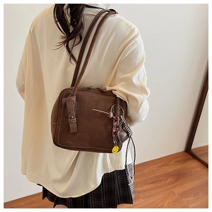 Brown suede tote bag detail with decorative charms and contrast stitching shown on shoulder