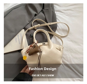 Detail view of off-white minimalist dumpling bag with decorative leather charms and strap