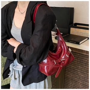 Close-up of a burgundy glossy leather hobo bag with side buckle straps and silver eyelets