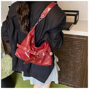 Close-up of a red patent leather shoulder bag with textured pleats and silver buckle