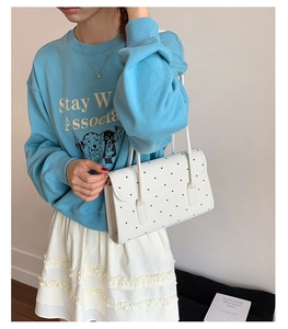 Close-up of white shoulder bag with black heart patterns and slim shoulder straps